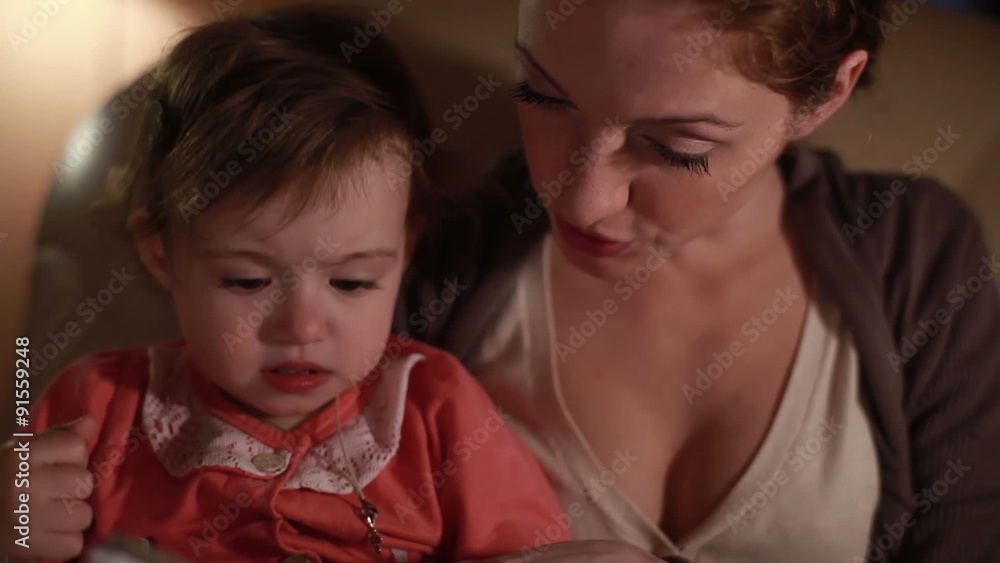 A young woman reading a book with her daughter late in the evening. A young woman reading a book with her daughter late in the evening.