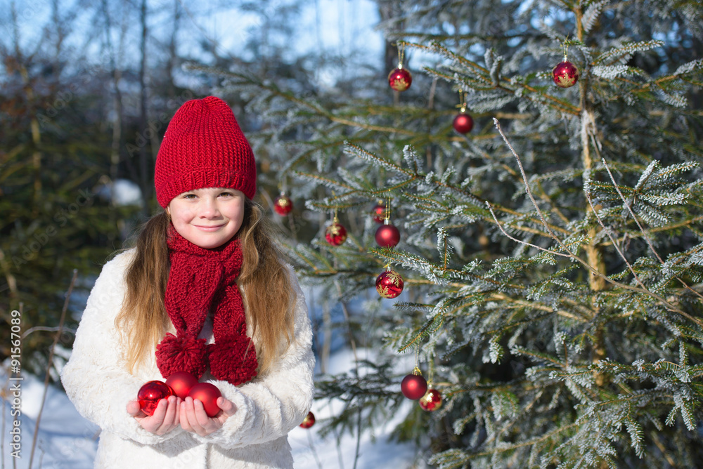 Smiling girl holding Christmas baubles in hands in the winter forest