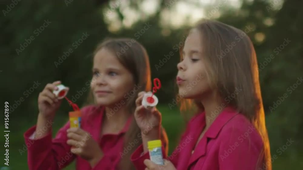Two Twin Girls are Playing with Soap Bubbles at Park Two Twin Girls are Playing with Soap Bubbles at Park