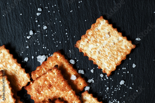 Crispy golden crackers with salt on dark stone background, top v