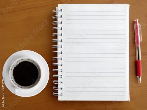 Notebook, pen and cup of coffee on wooden table