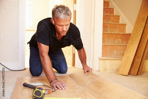 Man laying wood panel flooring during a house refurbishment