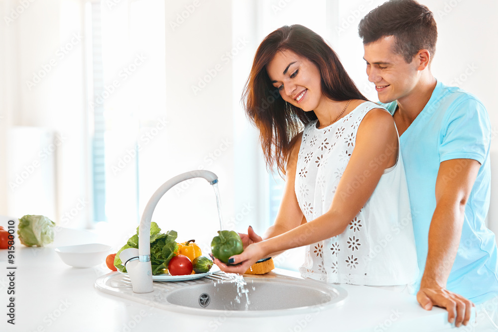 Woman washing vegetables, man hugging her  in kitchen