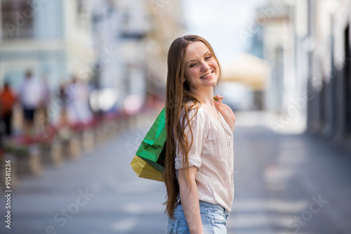 Happy beautiful woman with colorful shopping bags in hand cheerfully walking down the street. Smiling at the camera 