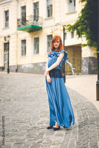redhead woman in blue dress standing on old street