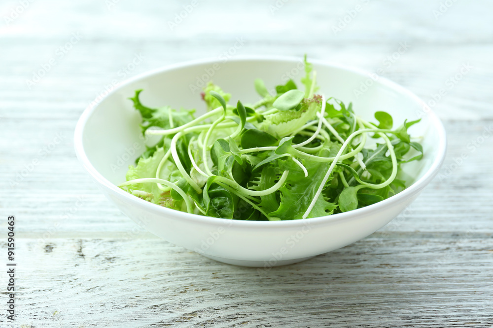 Fresh mixed green salad in bowl on wooden table close up Fresh mixed green salad in bowl on wooden table close up