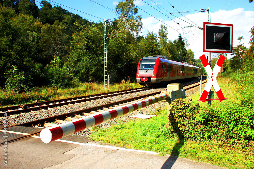 Fototapeta premium Zug nähert sich einem Bahnübergang mit geschlossener Schranke 