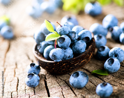 Blueberries in wooden bowl over rustic wooden table closeup
