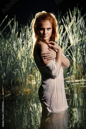 Foto Beautiful nymph in wet white chemise is standing in the night ri
