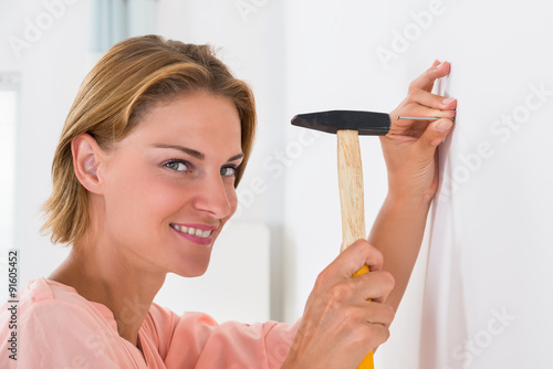 Young Woman Hitting Nail In A Wall