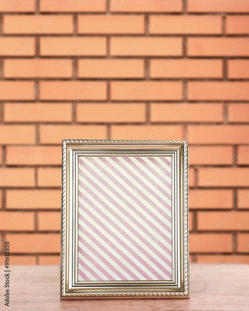 Fototapeta premium Old frame standing on table on brick wall background
