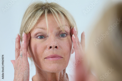 Senior woman looking at her skin in mirror