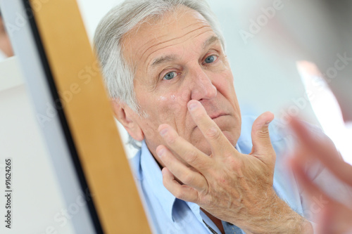 Senior man applying anti-aging lotion on his face