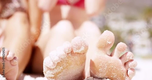 Close up of sandy feet wiggling toes three beautiful young woman sitting on tropical beach vacation