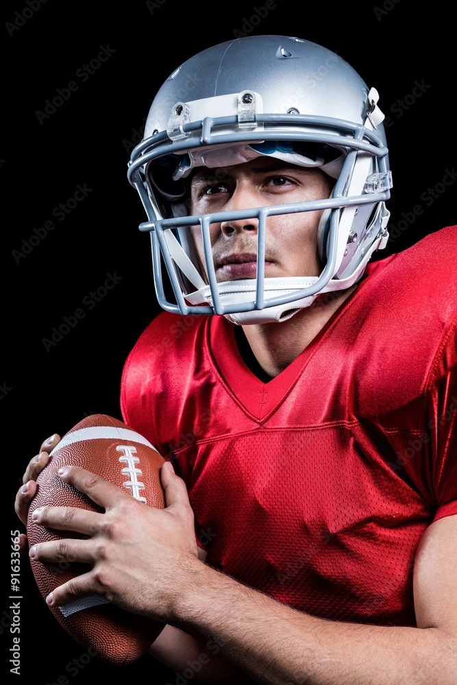 Serious American football player looking away while holding ball
