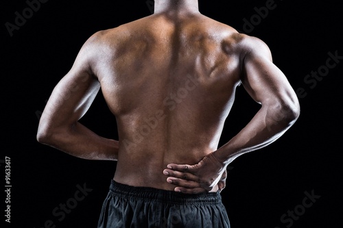 Mid section of muscular athlete suffering through back pain