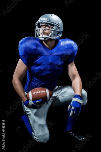 American football player with ball kneeling