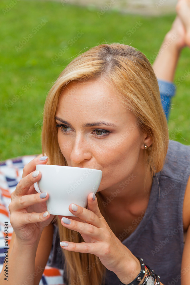 Sensual blonde woman lying in park on blanket. Outdoor photo. She is drinking coffee. Sensual blonde woman lying in park on blanket. Outdoor photo. She is drinking coffee.