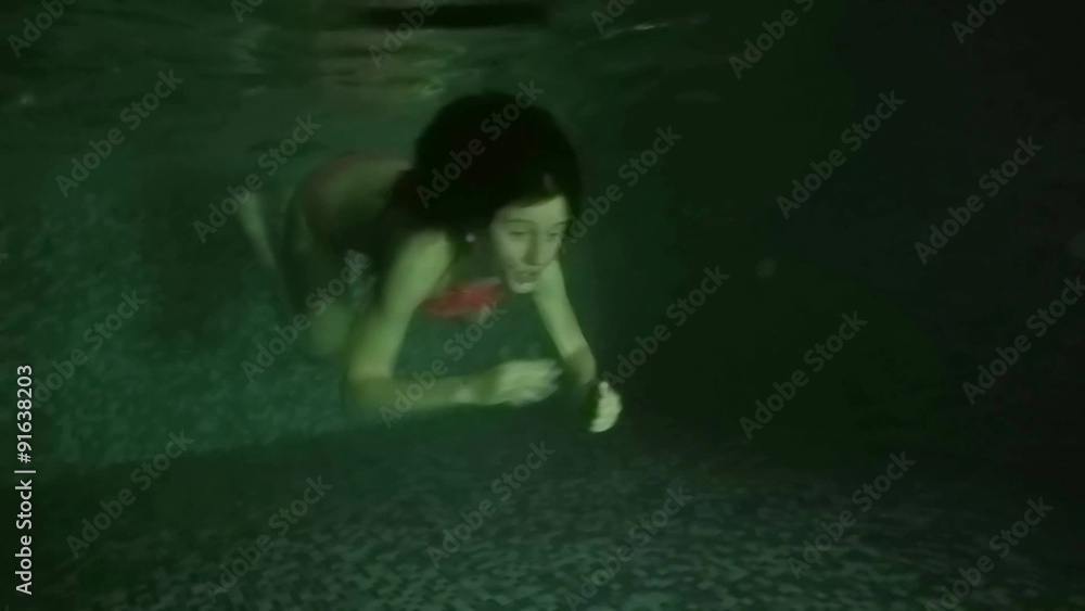 Underwater view of swimming girl in dark pool side view. UHD 4K stock footage Underwater view of swimming girl in dark pool side view. UHD 4K stock footage