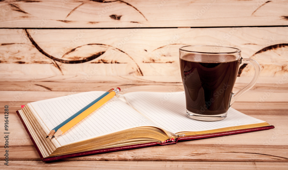 Naklejka premium cup of espresso, checkered notebook and bun on wooden background