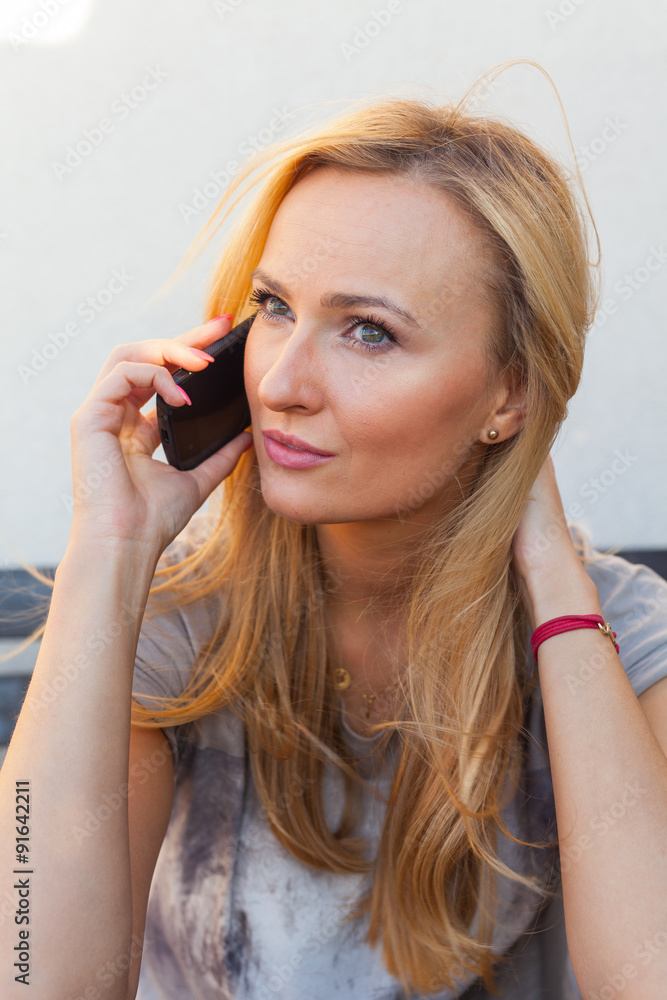 Sensual blonde woman sitting on wooden bench. She is using mobile phone. Sensual blonde woman sitting on wooden bench. She is using mobile phone.