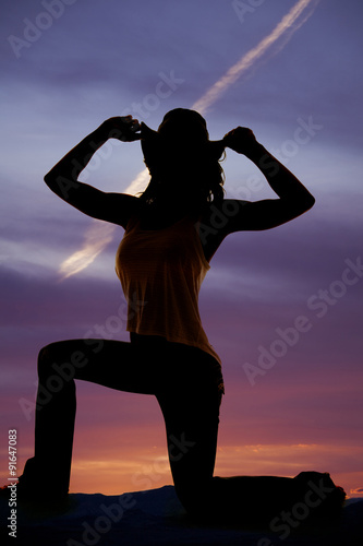 silhouette of a cowgirl kneel on one knee hands on hat