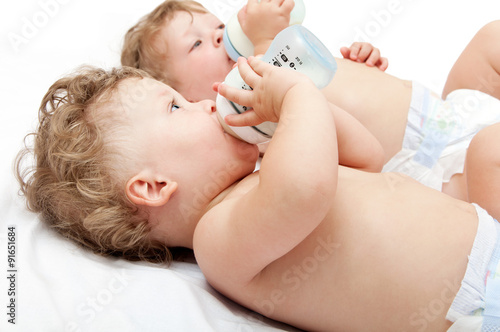 children twins lying suck milk bottles on white background