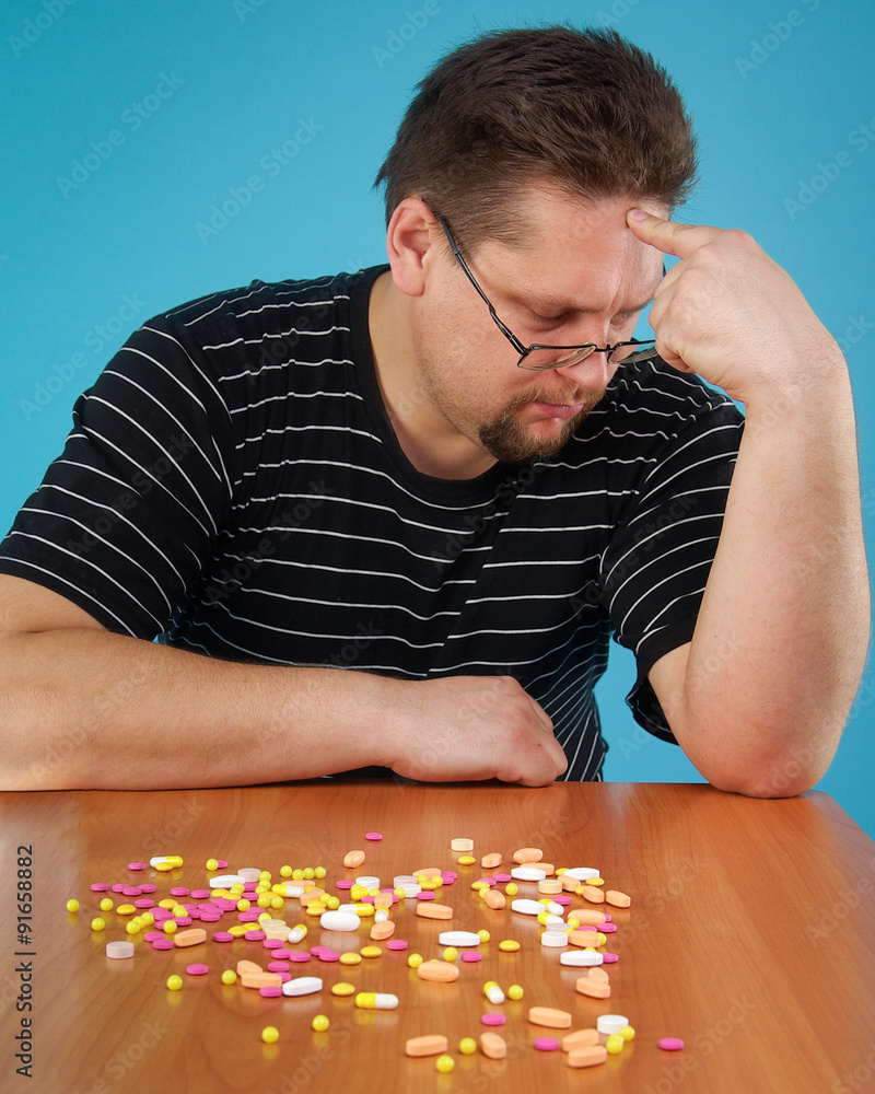 Мужчина задумался глядя на гору таблеток. Разноцветные таблетки на ...