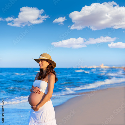 Beautiful pregnant woman on the beach with hat