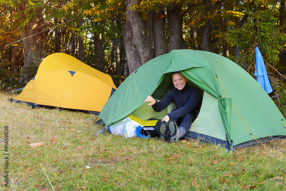 Laughing hiker woman is resting in tent in autumn mountains.