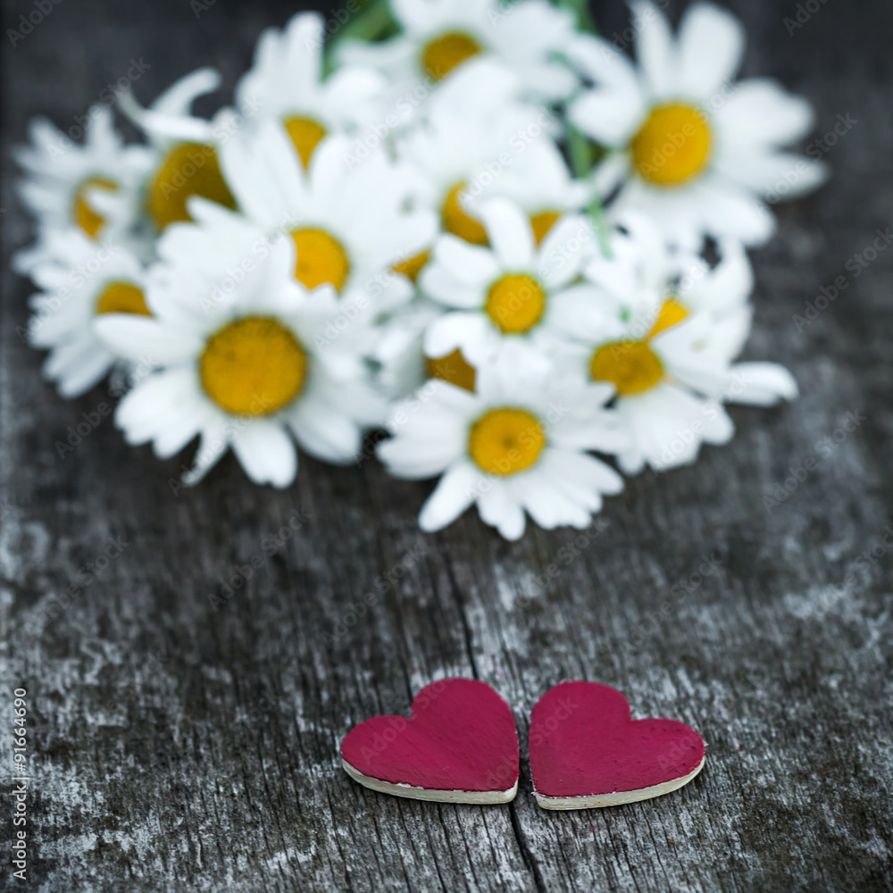 Fototapeta premium Beautiful fresh daisies decorated with hearts on wooden texture