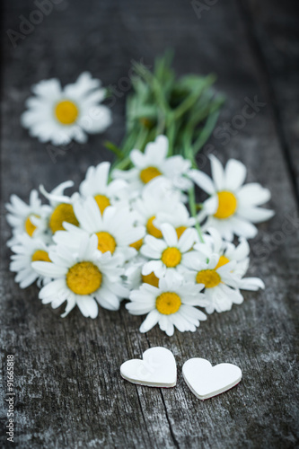 Beautiful fresh daisies decorated with hearts on wooden texture