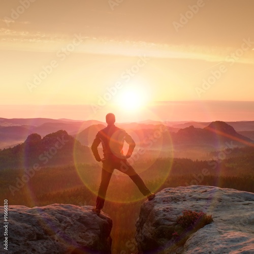 Jumping hiker in black celebrate triumph between two rocky peaks. Wonderful daybreak with sun above head..