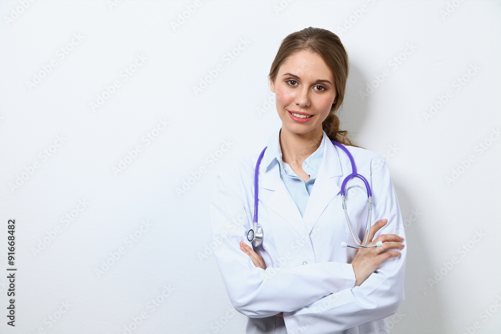 Friendly smiling young female doctor, standing near wall Friendly smiling young female doctor, standing near wall