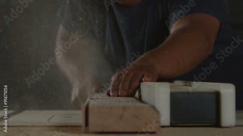 A woodworker saws a plank on a workbench.