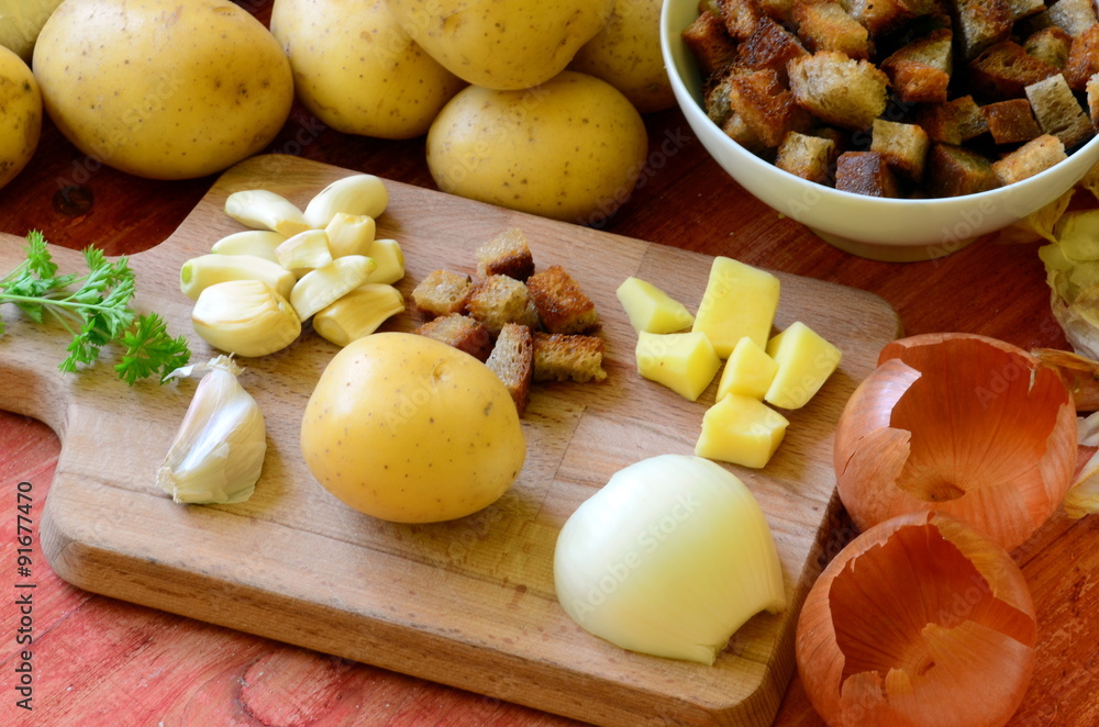 Ingredients for garlic soup on chopping board - potatoes, onion, garlic, roasted bread, parsley Ingredients for garlic soup on chopping board - potatoes, onion, garlic, roasted bread, parsley