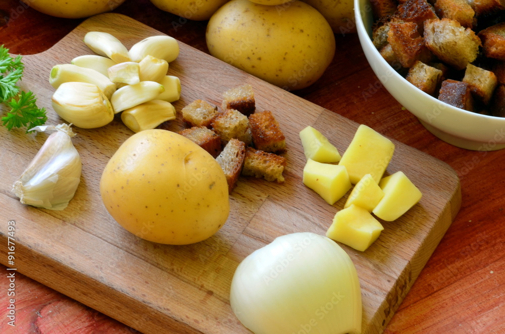 Ingredients for garlic soup on chopping board - potatoes, onion, garlic, roasted bread, parsley Ingredients for garlic soup on chopping board - potatoes, onion, garlic, roasted bread, parsley