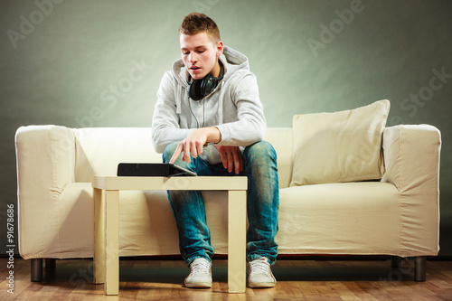 man with headphones sitting on couch with tablet © Voyagerix