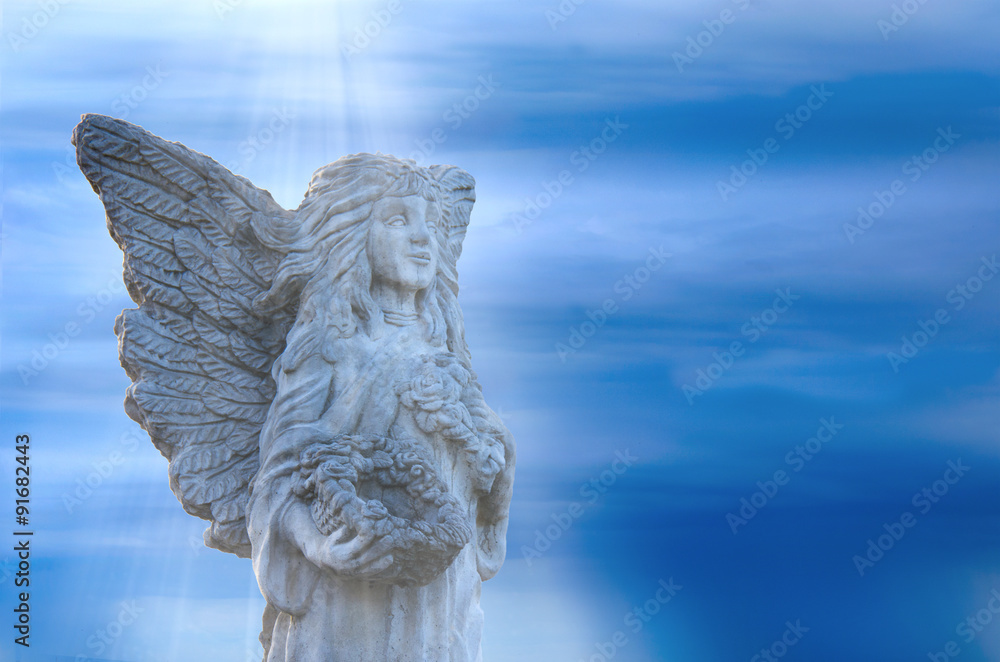 Stone angel statue standing within soft light beams from Heaven with a stormy background. The angel is holding a flower rimmed basket while clutching a rose up to her breast.