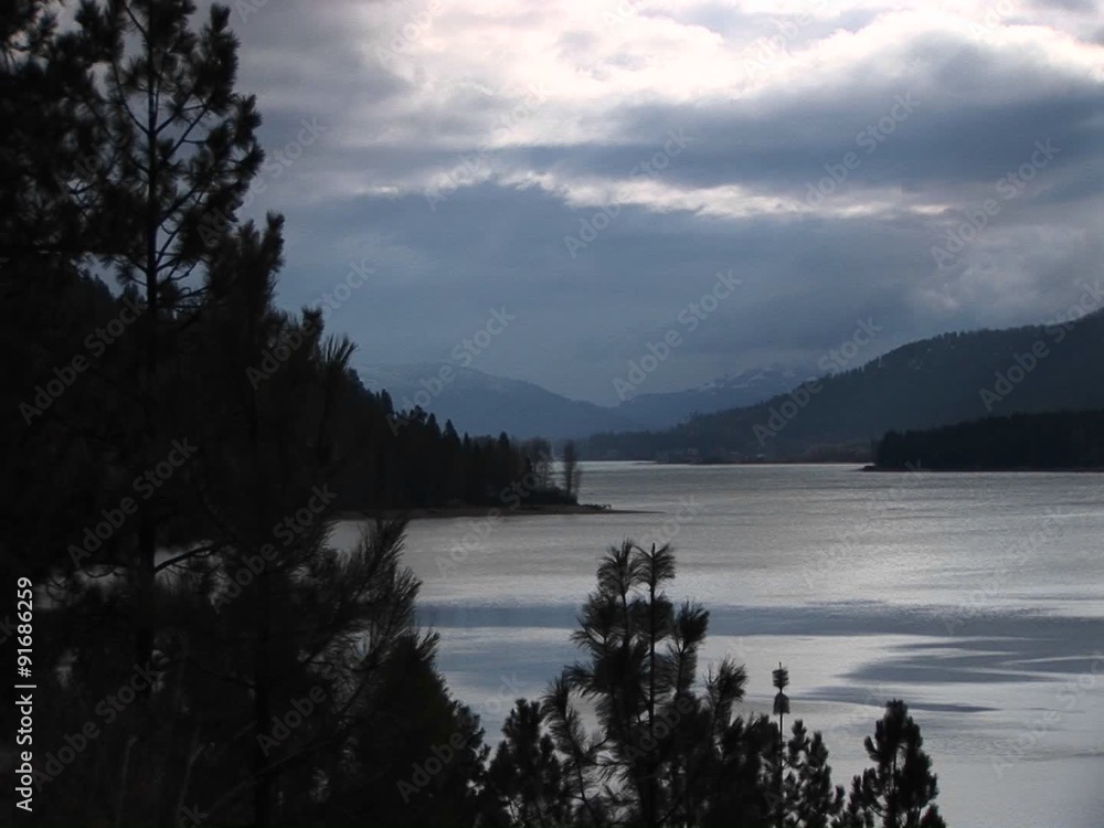A scenic view of an ocean inlet and shoreline with trees and hills in grays and blues. A scenic view of an ocean inlet and shoreline with trees and hills in grays and blues.