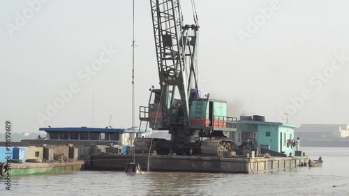 DREDGING RIVER: Wider shot crane scoops sand from river in giant bucket; from StockFootageWorld