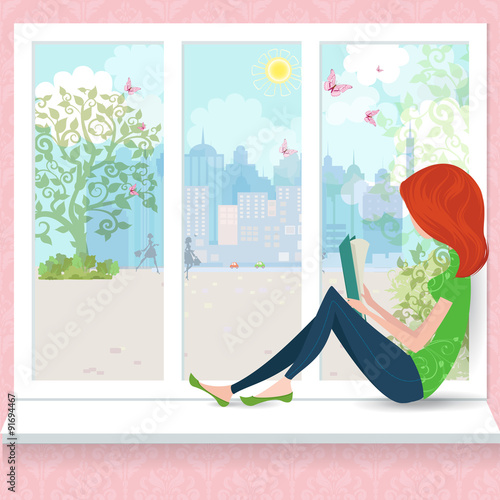 Cute girl is reading a book on a window sill.