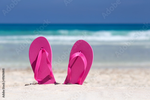 Pink flip flops on sandy beach near sea. Summer vacation concept