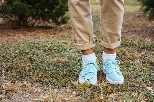 Female feet in beige pants and a turquoise sneakers standing on
