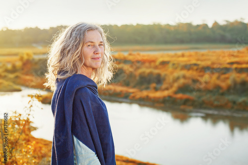 Beautiful mature woman standing in front of the river in autumn