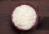 Bowl with uncooked rice on wooden table seen from above