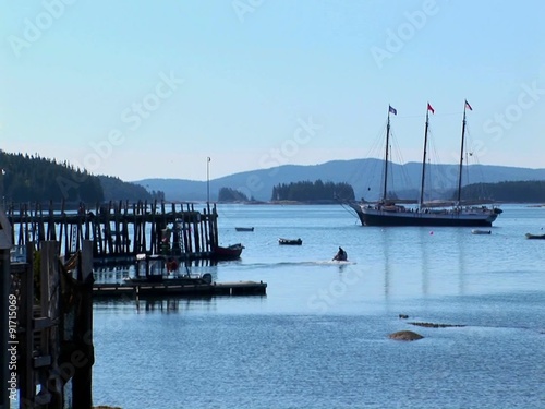 A sailing ship is at anchor near a wooden pier offshore a lobster village in Stonington, Maine. photo