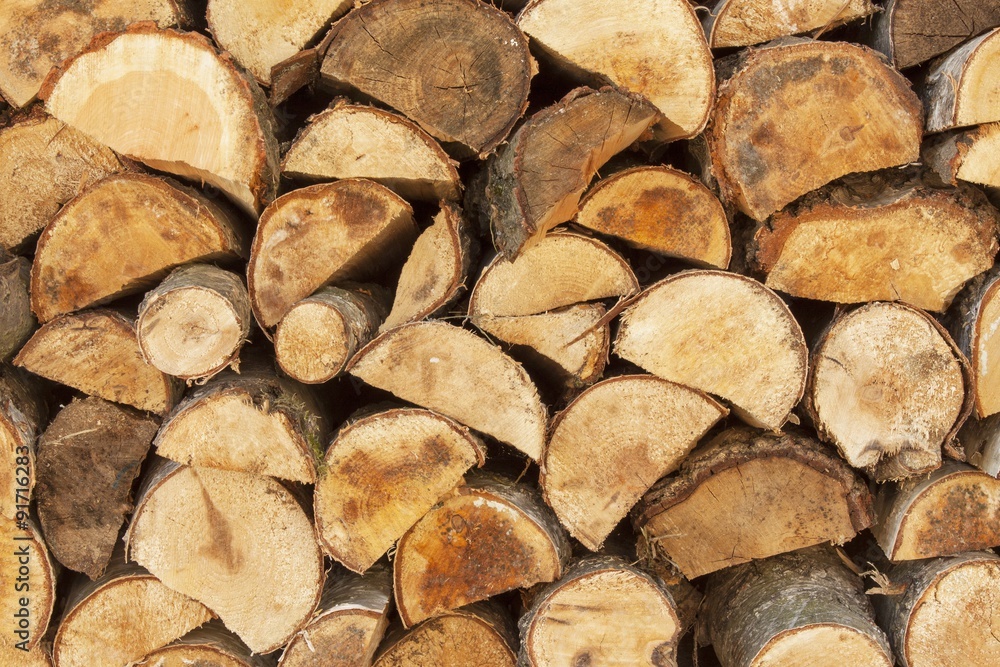 Fototapeta premium Background of stacked wood. Ready firewood. Various kinds of wooden logs stacked on top of each other. Stack of wood, firewood, background. Dry chopped firewood logs ready for winter.