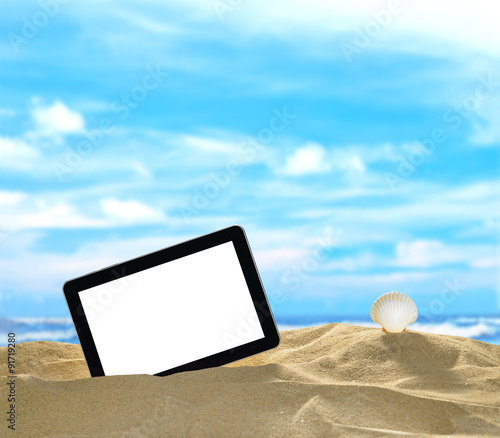 Tablet computer and seashells on the beach with blue sea and sky