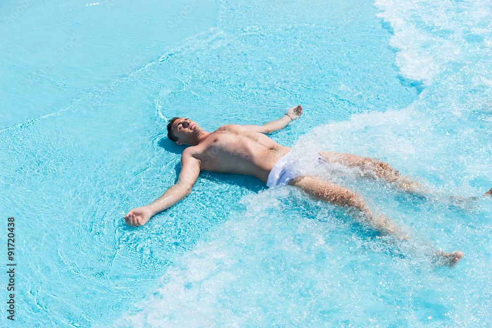 Young Man Lying on Back in Shallow Waves of Pool